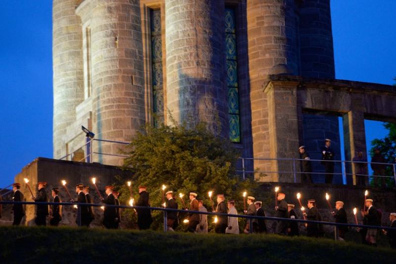 Freitagabend in Eisenach: Etwa 400 Korporierte stampfen schweigend mit Fackeln in den Händen zu einem etwa 30 Meter hohen Turm mit Blick auf die Wartburg, der sich düster über die Stadt erhebt.